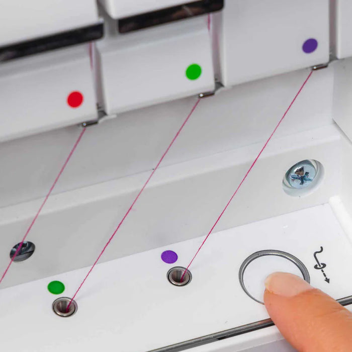 Close-up of a sewing machine needle threader with colored buttons and a finger pressing a button.