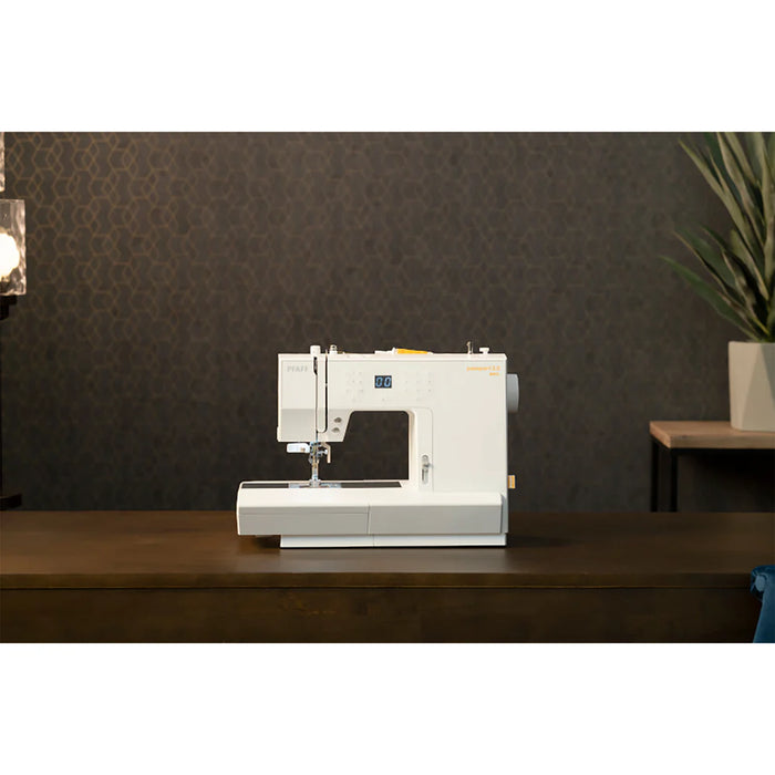 White sewing machine on a wooden surface with a dark wall and plant in the background