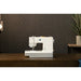 White sewing machine on a wooden surface with a dark wall and plant in the background