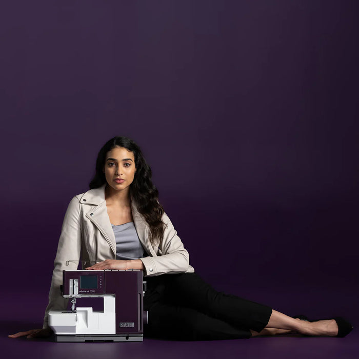 Woman sitting on a purple floor with a sewing machine in front of a purple background