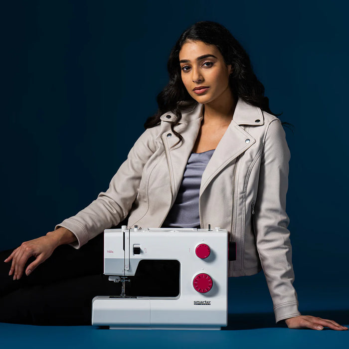 Woman sitting next to a sewing machine on a dark background