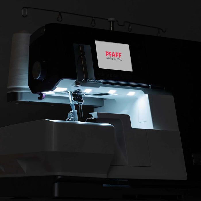 Sewing machine with a lit screen displaying 'PFAFF' in a dark setting