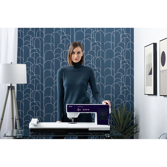 Woman holding a sewing machine in a room with decorative wall and decor.