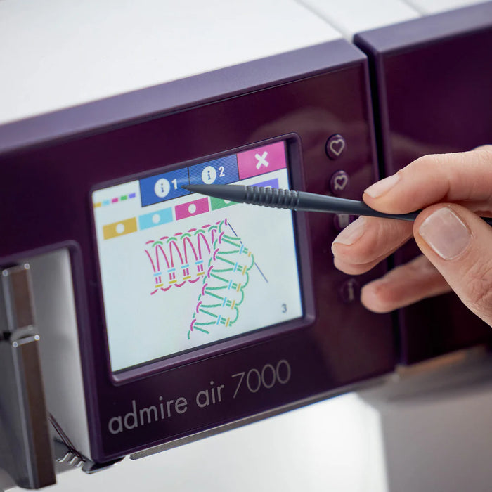 Person using a stylus to interact with the touchscreen of a embroidery machine labeled 'admire air 7000'.