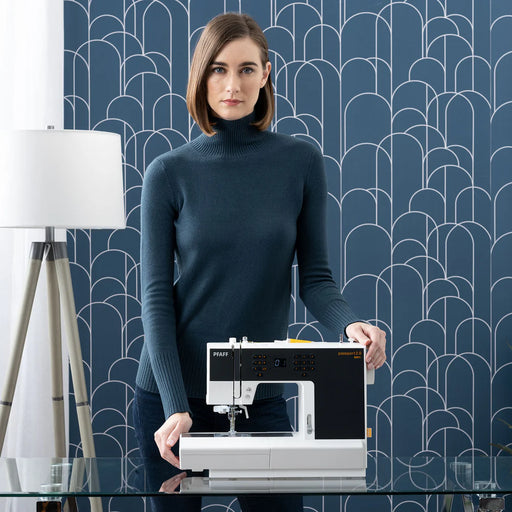 Woman standing behind a sewing machine against a blue geometric-patterned wall.