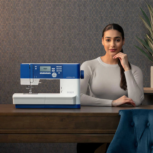 Woman sitting at a table with a blue and white sewing machine against a patterned wall.
