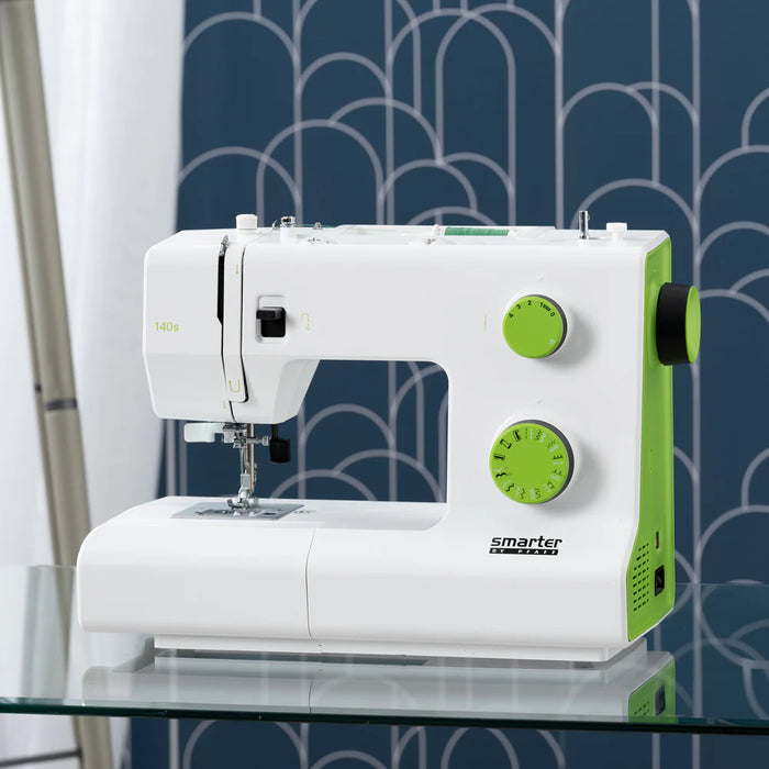 White and green sewing machine on a glass surface with a patterned wall in the background