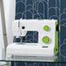 White and green sewing machine on a glass surface with a patterned wall in the background