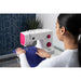Woman using a white and pink sewing machine in a home setting.