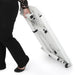 Person transporting the folded Arrow Gidget II Sewing Table 611 using its built-in wheels for mobility.