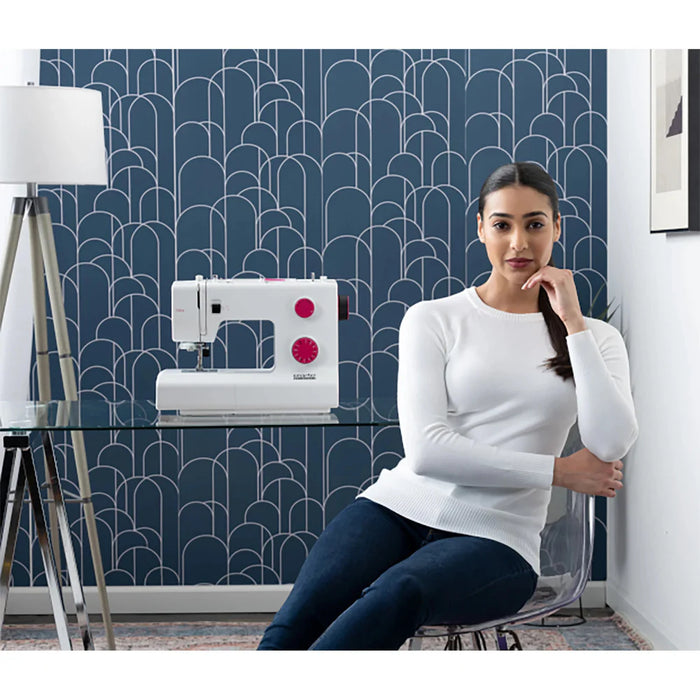 Woman sitting next to a sewing machine in a room with geometric wallpaper.