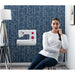 Woman sitting next to a sewing machine in a room with geometric wallpaper.