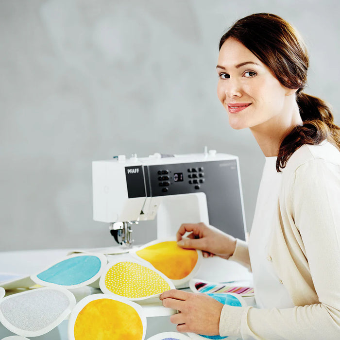 Woman working with colorful fabric samples in front of a Pfaff sewing machine.