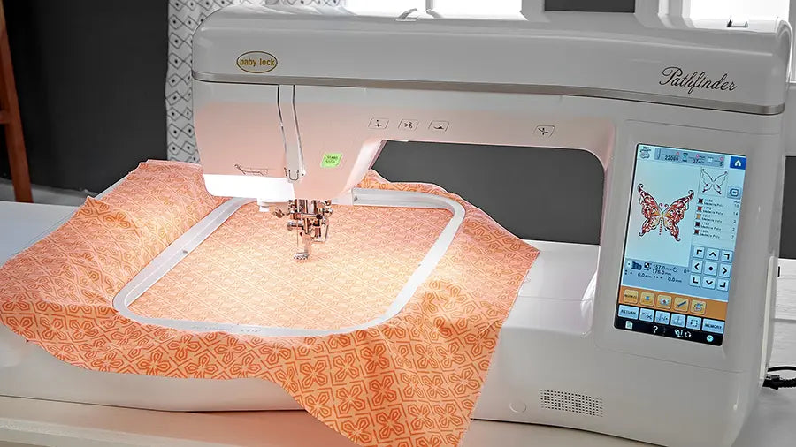 Baby Lock Pathfinder BLPF embroidering butterfly design on orange patterned fabric using bright touchscreen display.