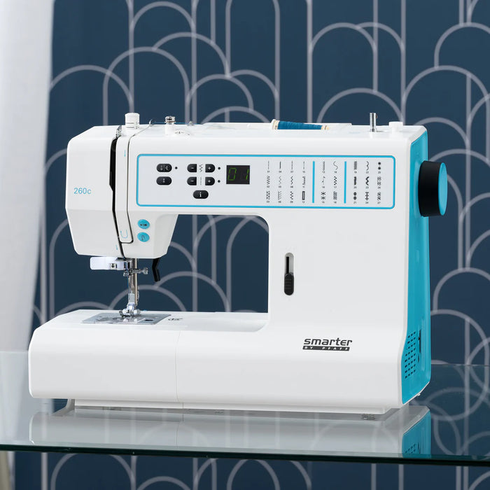 White and blue sewing machine on a glass surface with a patterned blue background
