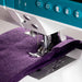 Sewing machine stitching purple fabric on a white background