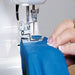 Close-up of Janome 1000CPX needles and presser foot stitching stretch fabric for clean, professional hems.