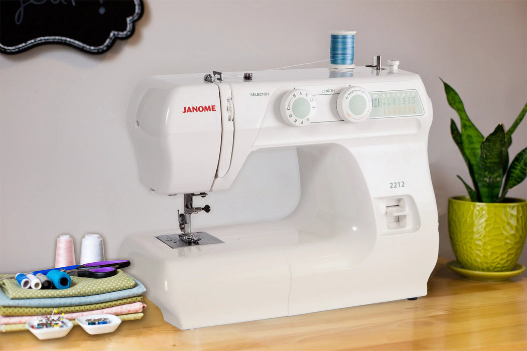 Janome 2212 Sewing Machine displayed on a sewing table with thread and fabric, ideal for beginner sewing projects.
