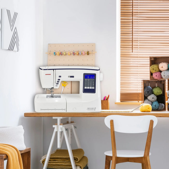 Janome Skyline S3 Anniversary Edition displayed in a home sewing room setup with yarn and crafting supplies.
