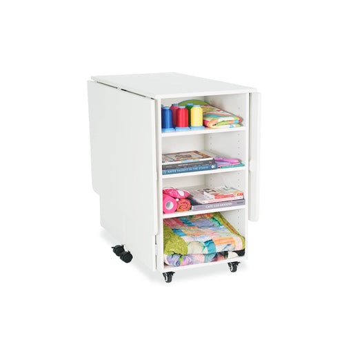 Kangaroo Kookaburra Cutting Table in ash white finish folded into compact storage position, showing accessible shelving for fabric, books, and sewing tools.
