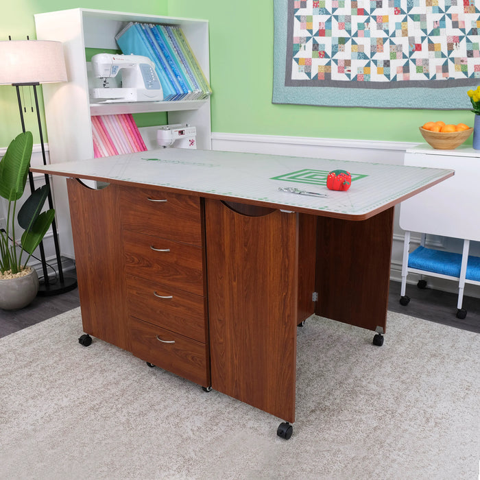 Kangaroo Kookaburra Cutting Table fully opened in a sewing room, displaying large cutting surface and front drawer storage in teak finish.
