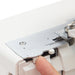 Close-up of a sewing machine needle plate with a hand adjusting it on a white background