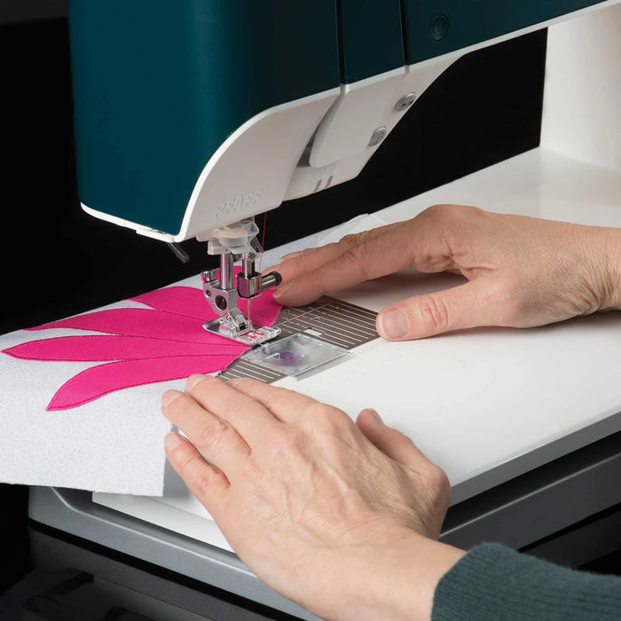 Person using a sewing machine to stitch a pink flower design on fabric.