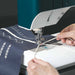 Person using a sewing machine on a piece of fabric with embroidery designs.