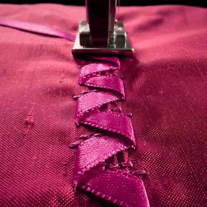 Close-up of a sewing machine needle stitching pink fabric.