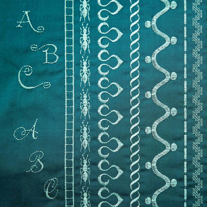Teal fabric with white embroidery patterns including letters, leaves, and abstract designs.